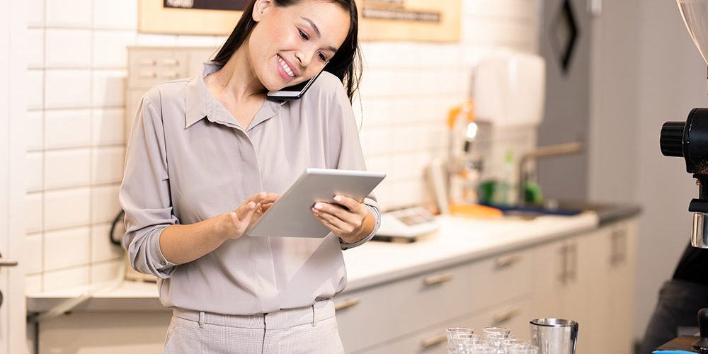 Happy young waitress working with orders of clients on the phone and online