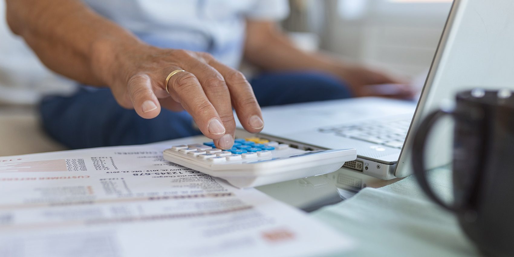 Serious elder senior grey-haired grandpa using calculator counting bank loan payment holding papers at home, focused mature old man doing paperwork calculating bills managing finances sit on sofa